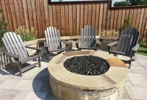 A fire pit with chairs around it and a wooden fence in the background.