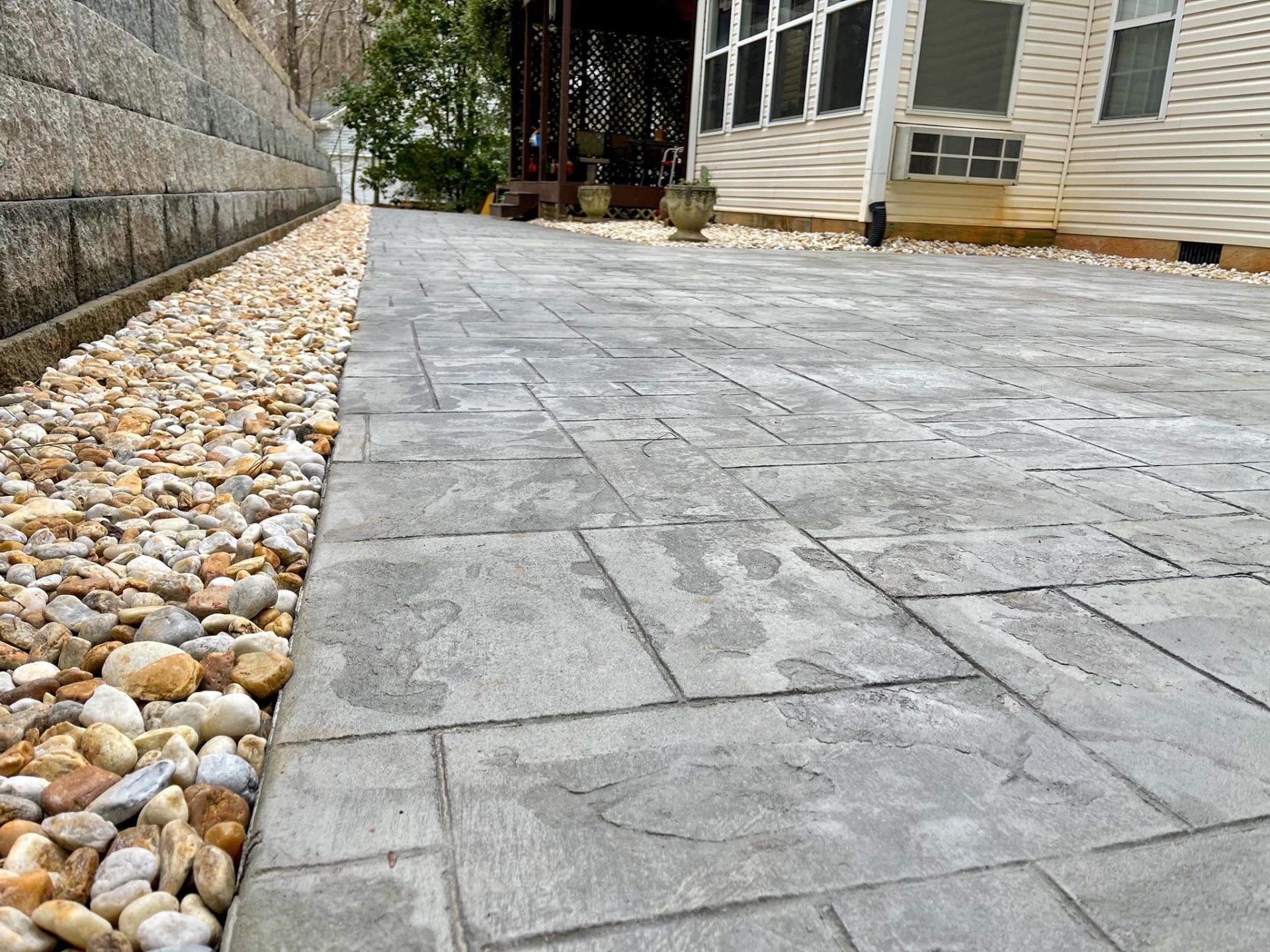 A brick driveway with gravel on the side of it and a house in the background.