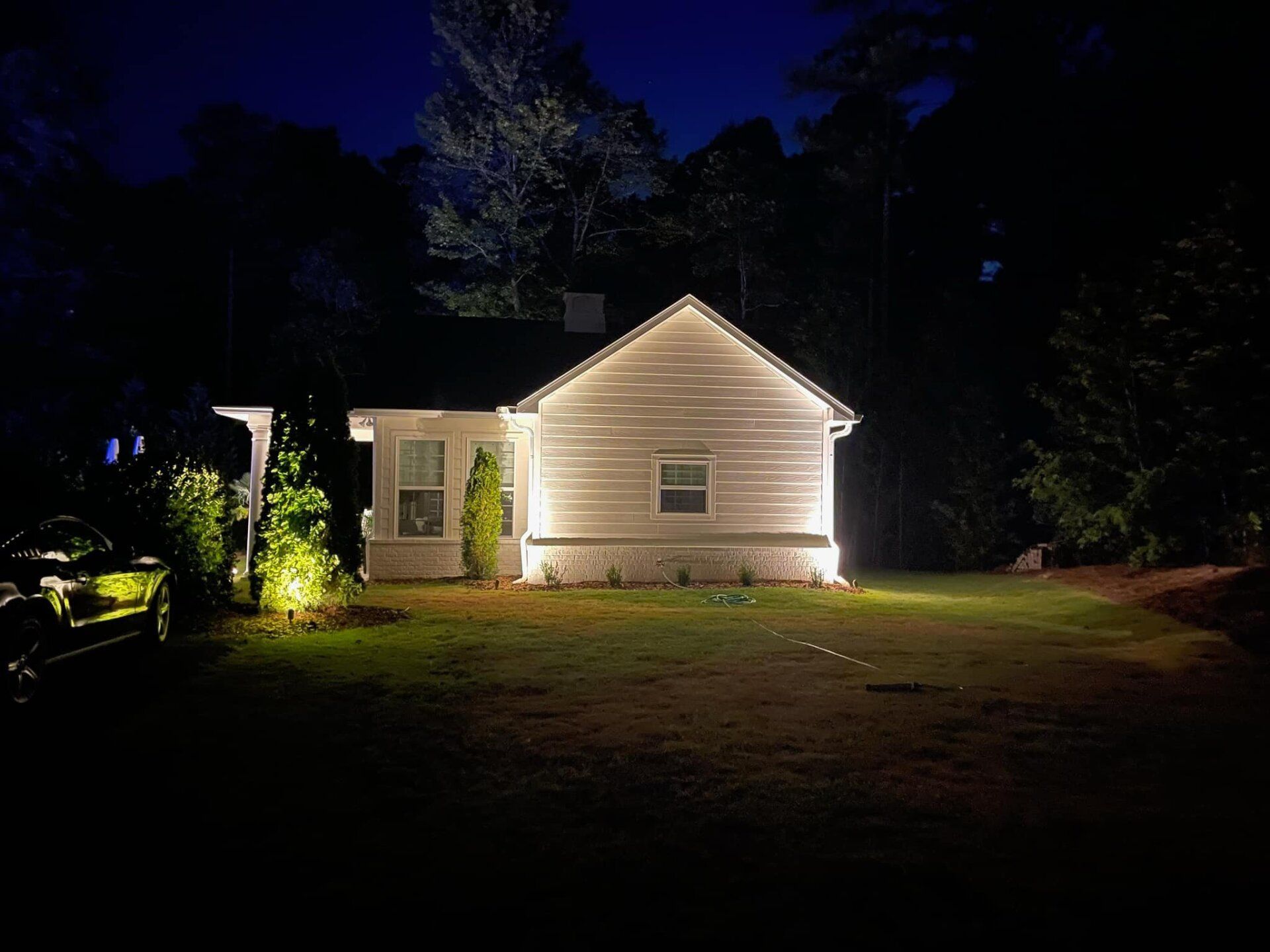 A white house is lit up at night with trees in the background
