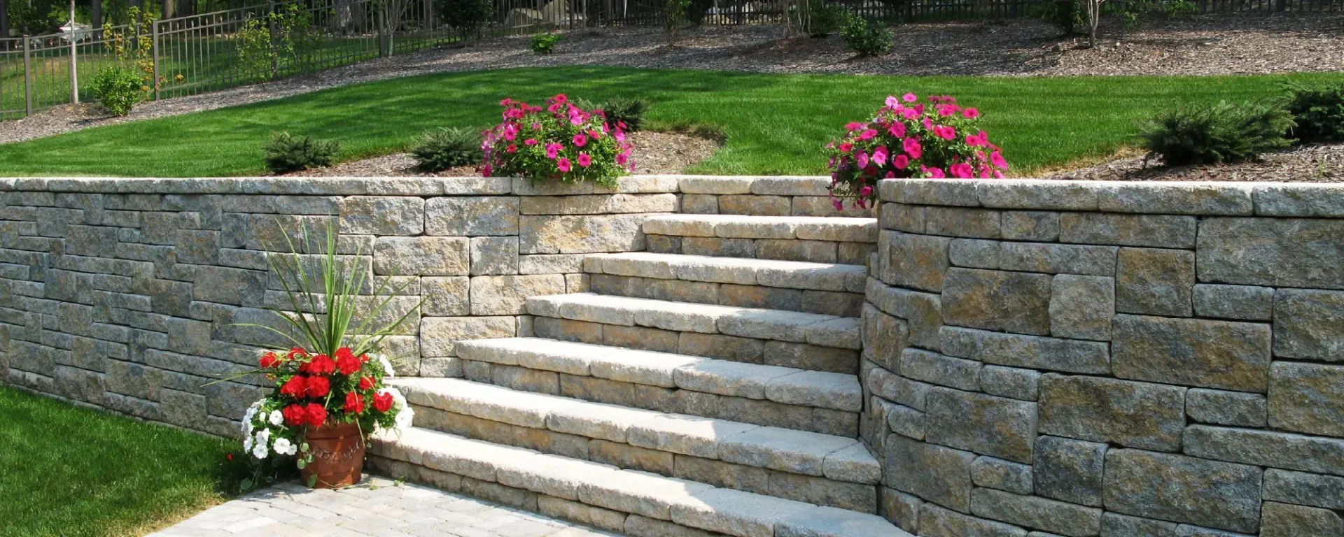 A stone wall with stairs leading up to it and flowers in a pot.