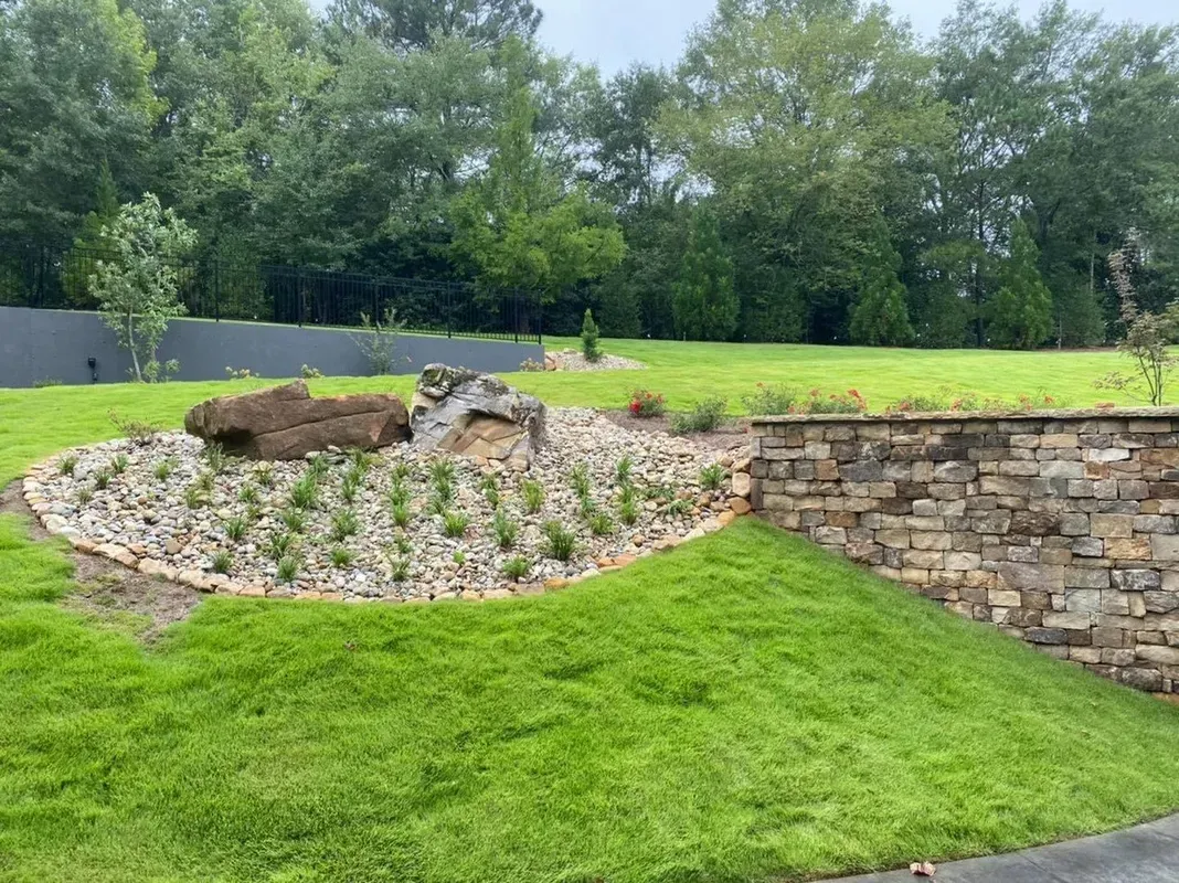 A lush green lawn with a stone wall in the background and trees in the background.