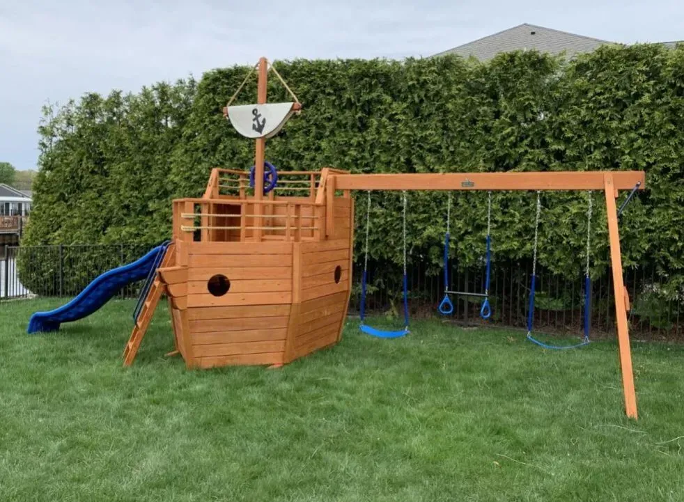 A wooden playset in the shape of a pirate ship with a slide and swings.