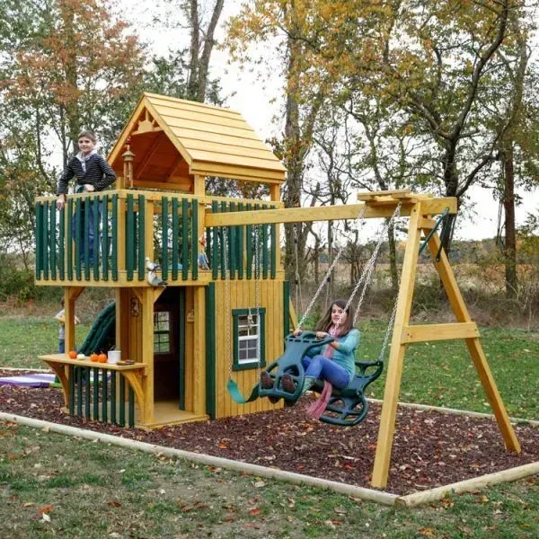 A woman sits on a swing in front of a wooden playhouse.
