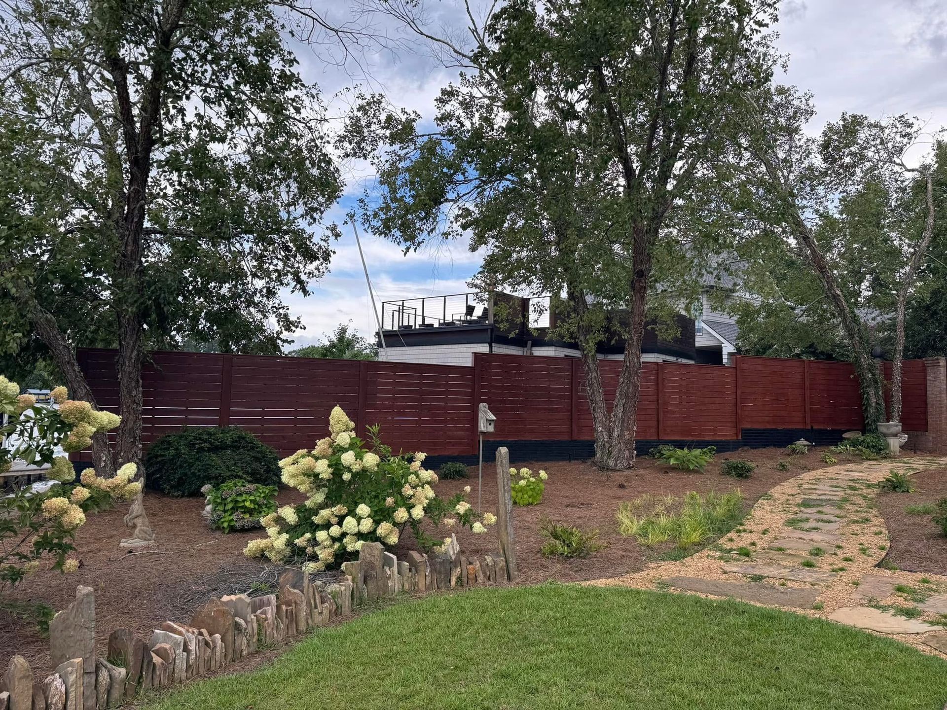 A wooden fence lines a yard with landscaping and trees. The sky is overcast.