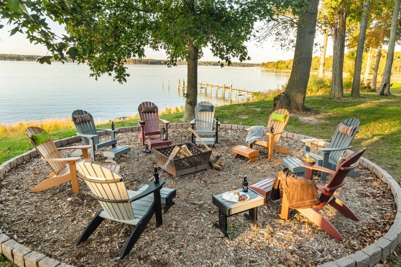 Circle of Adirondack chairs around a fire pit by a lake.