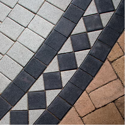 Close-up of a paved surface with gray, black, and tan bricks arranged in patterns.