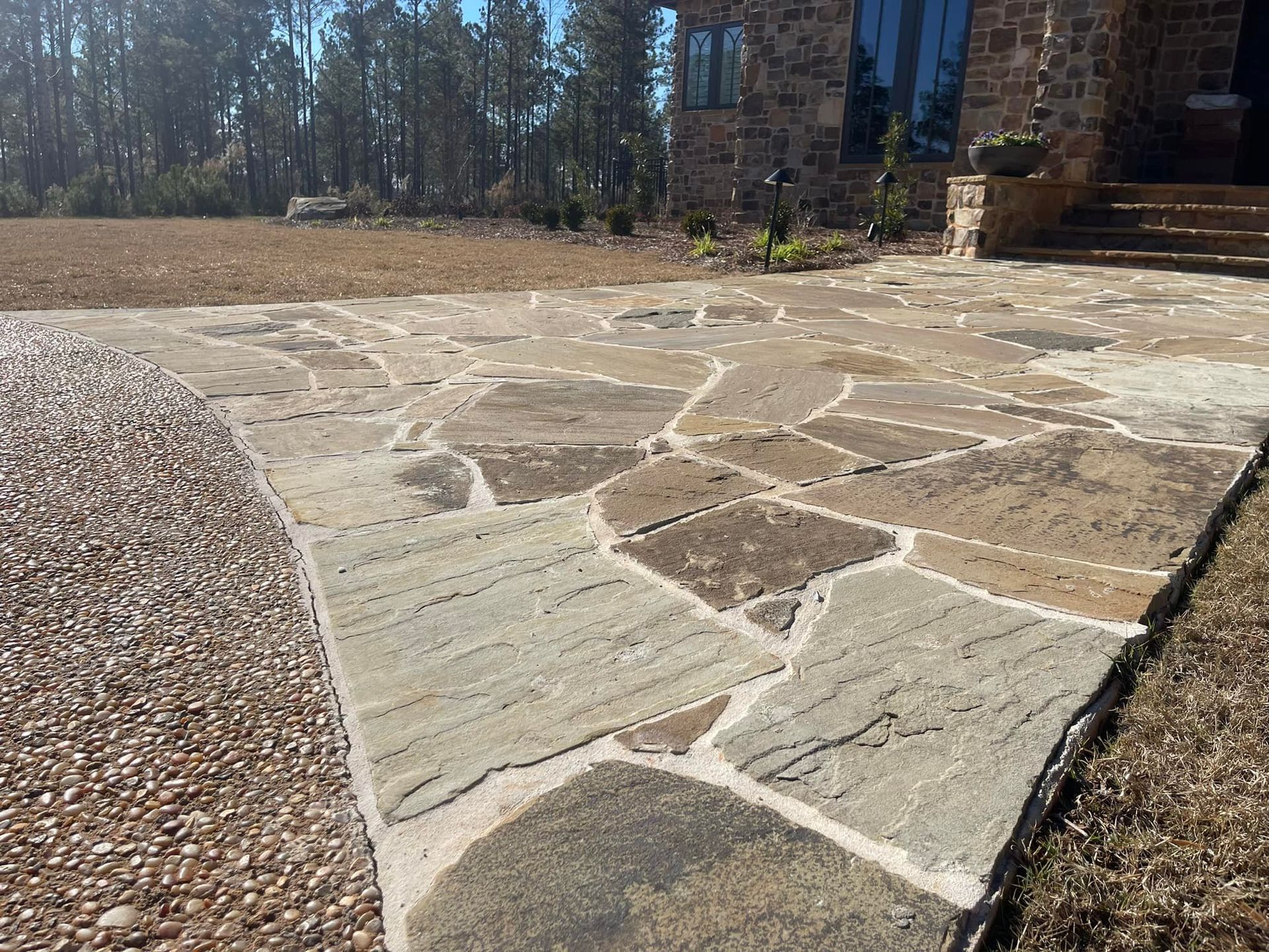 Stone walkway leading to a stone building entrance with stairs, surrounded by gravel and grass.