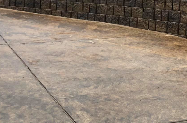Concrete driveway next to a retaining wall made of dark brick blocks.