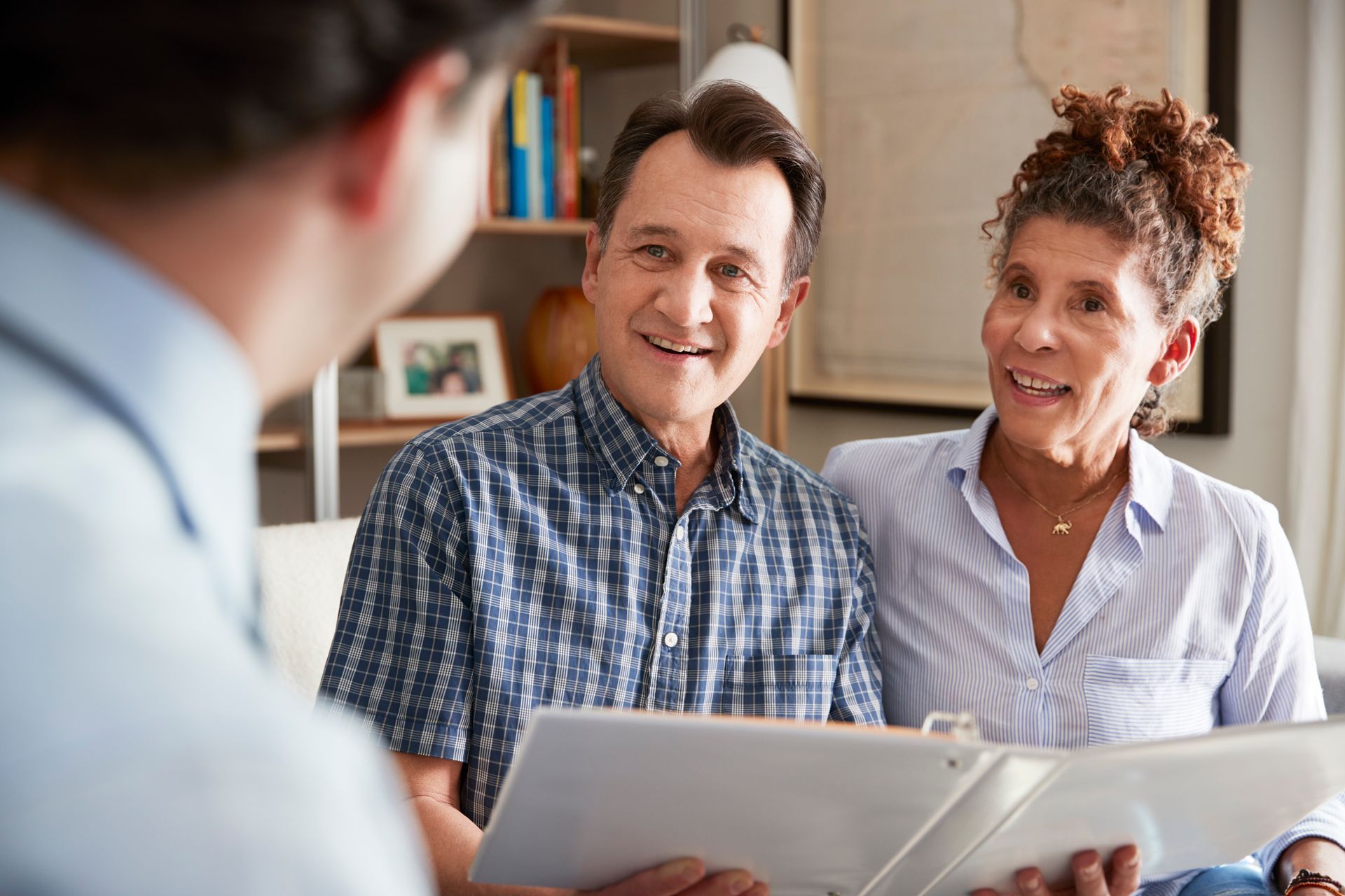 Couple reviewing a document with a person, indoors. They smile, looking at the person who is holding the document.