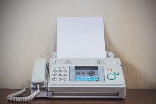 a fax machine is sitting on a wooden table with a piece of paper coming out of it .