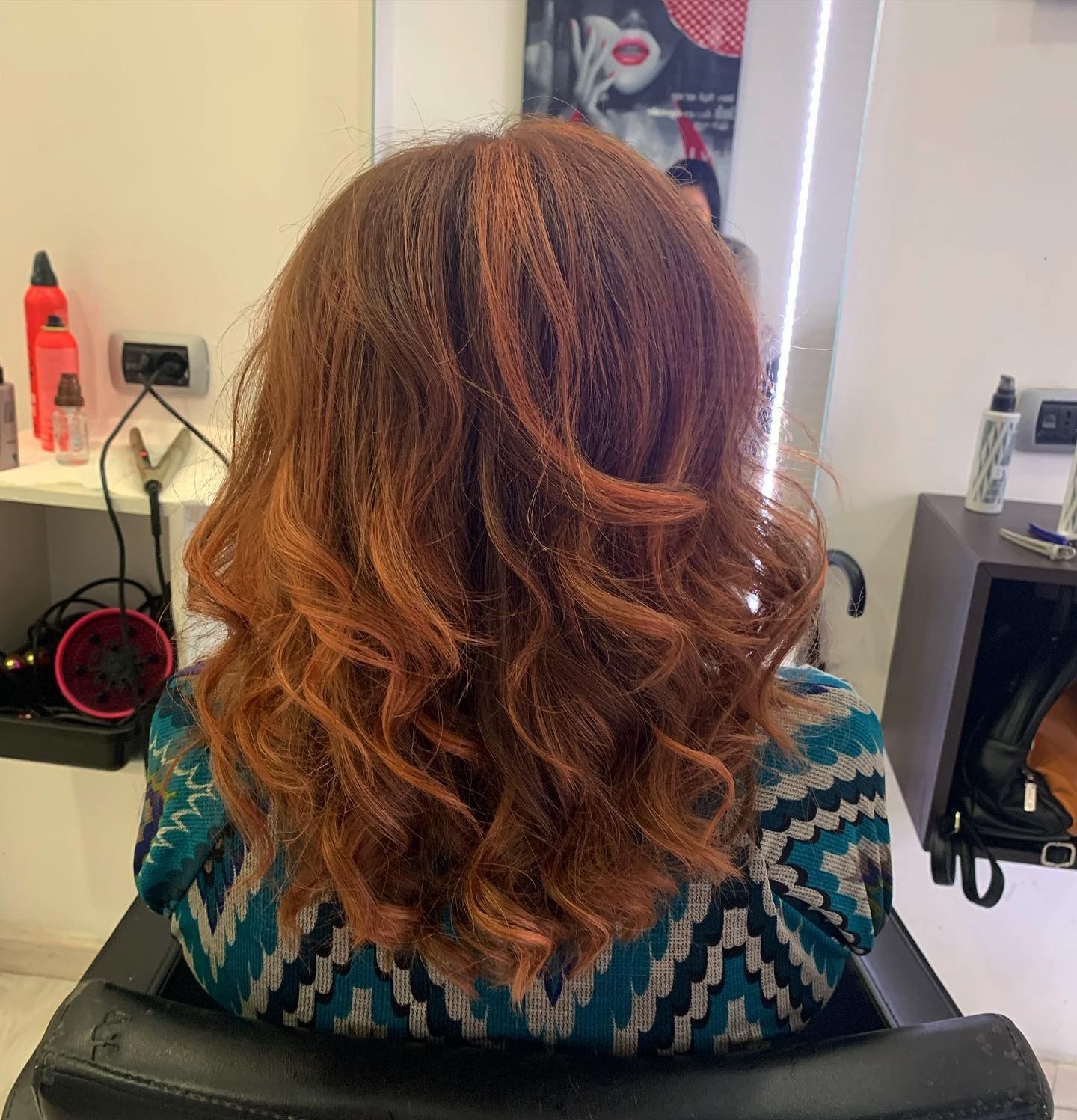 Donna con lunghi capelli ondulati, castano-rossicci, che indossa un maglione verde acqua, in un salone di bellezza.