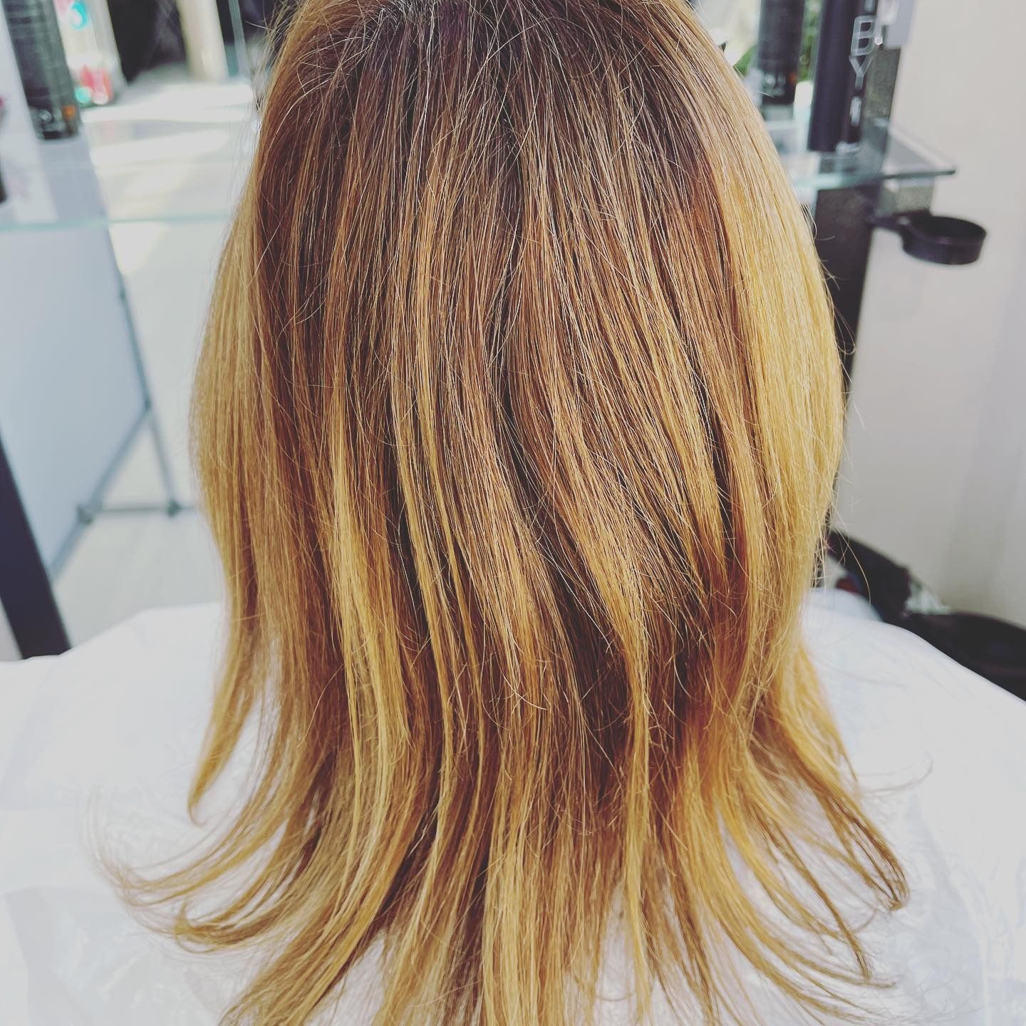 Capelli di una donna, acconciati con mèches bionde e radici scure, in un salone.