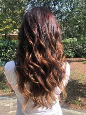 Donna con capelli castano scuro ondulati, effetto ombré che sfuma verso un castano più chiaro alle punte, all'aperto.