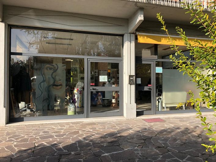 Un negozio con porte in vetro e grandi finestre che espongono gli articoli; edificio grigio con una tenda da sole gialla.