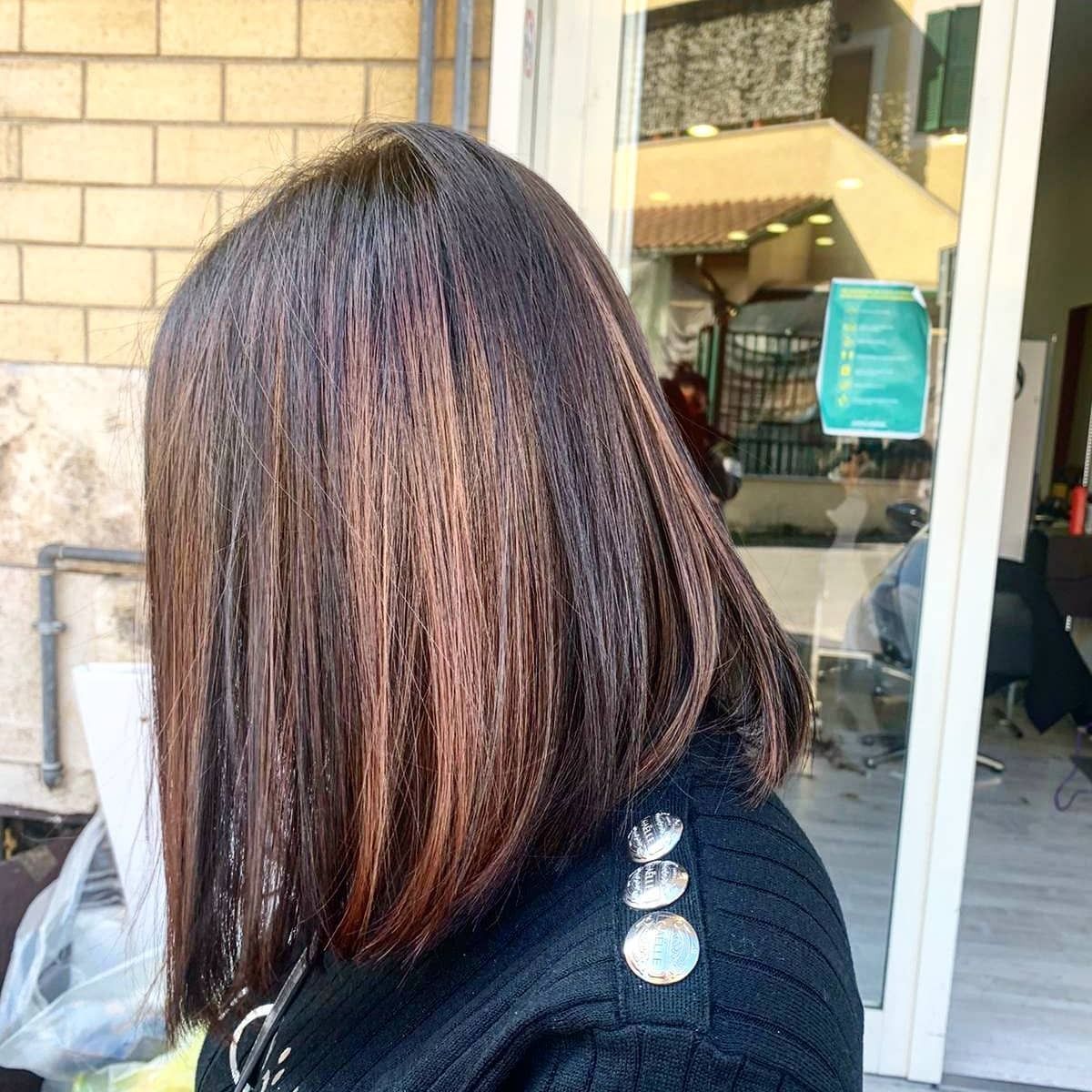 Donna con capelli scuri scalati, che indossa un maglione nero con bottoni argentati, in piedi vicino all'ingresso di un salone.