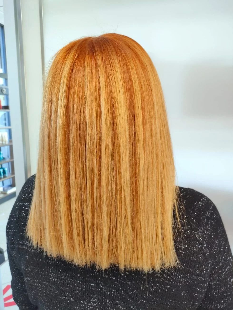 Donna con lunghi capelli lisci color arancio, acconciati con linee verticali testurizzate, indossa un top nero.