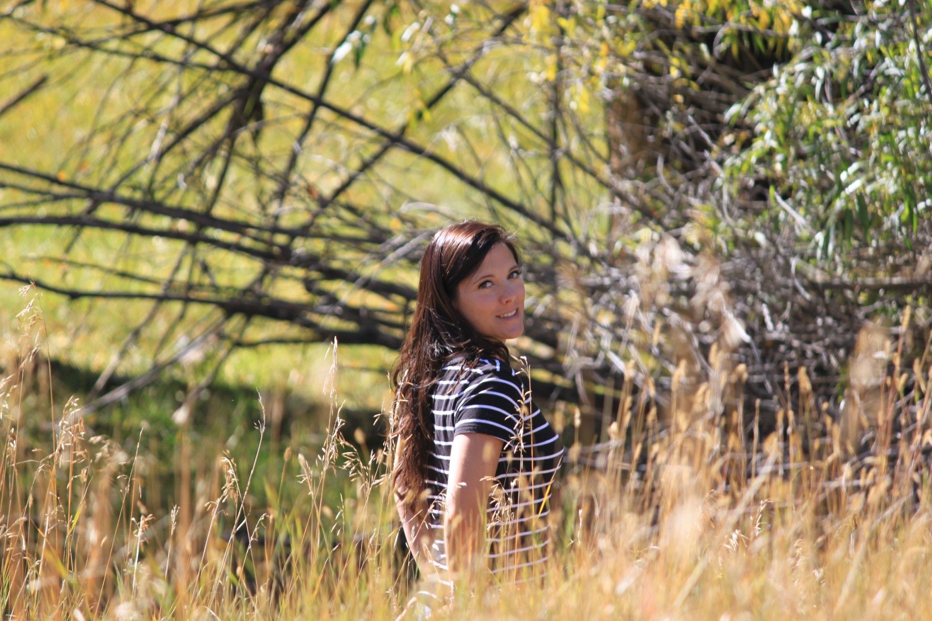 Woman in striped shirt looks over shoulder in tall grass.