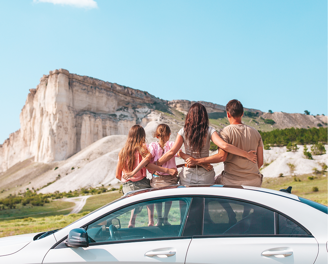 A group of people are sitting on the roof of a car.