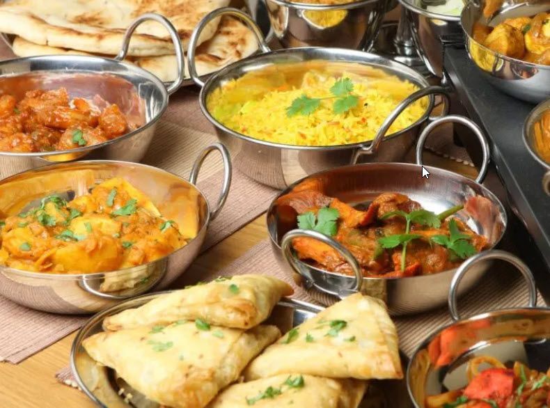A variety of indian food in stainless steel bowls on a table.