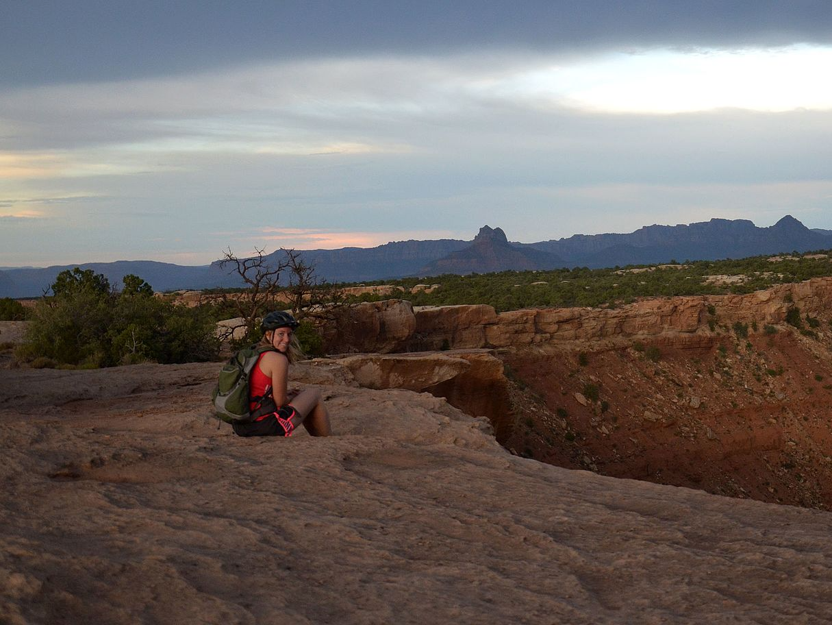 A person with a backpack is sitting on a rock in the desert.