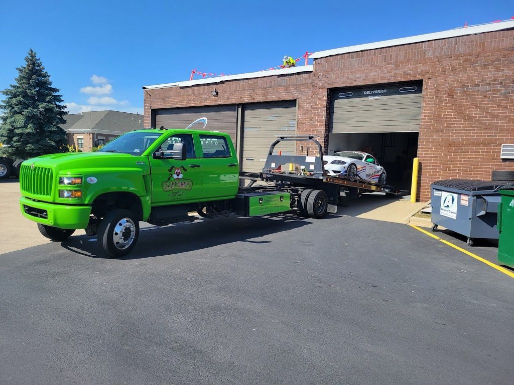 A green tow truck is parked in front of a brick building.