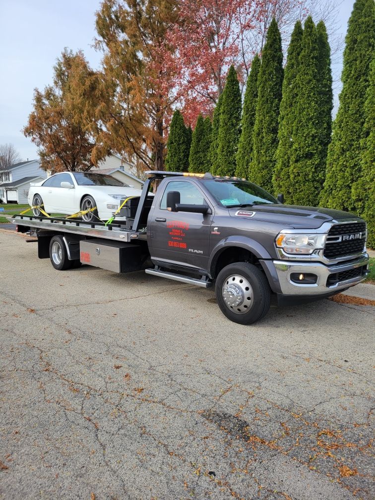 A tow truck with a white car on the back is parked on the side of the road.