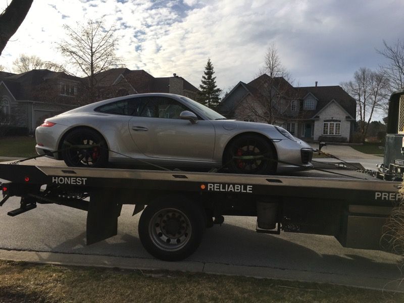 A silver porsche is sitting on top of a tow truck