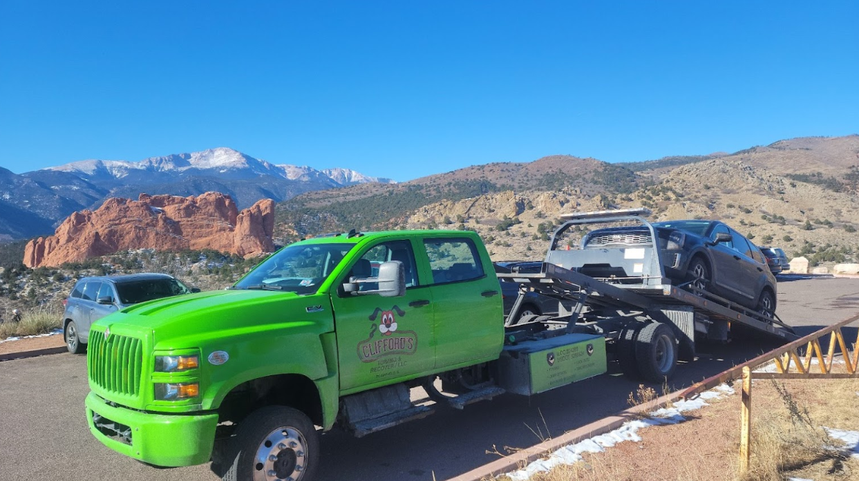 A green tow truck is towing a car in a parking lot.