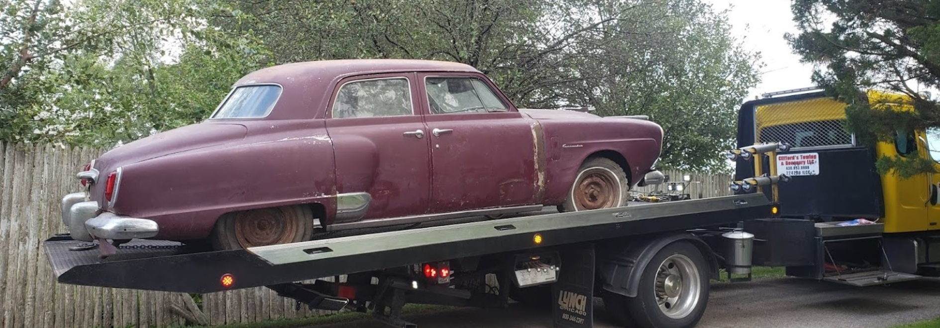An old car is being towed by a tow truck.