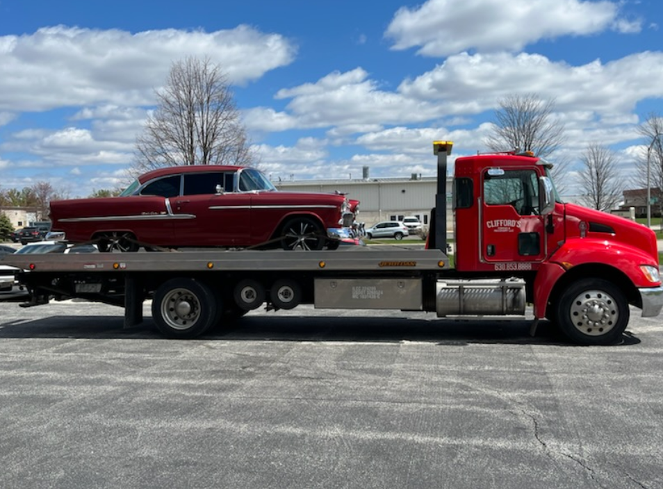 A red car is on the back of a tow truck.