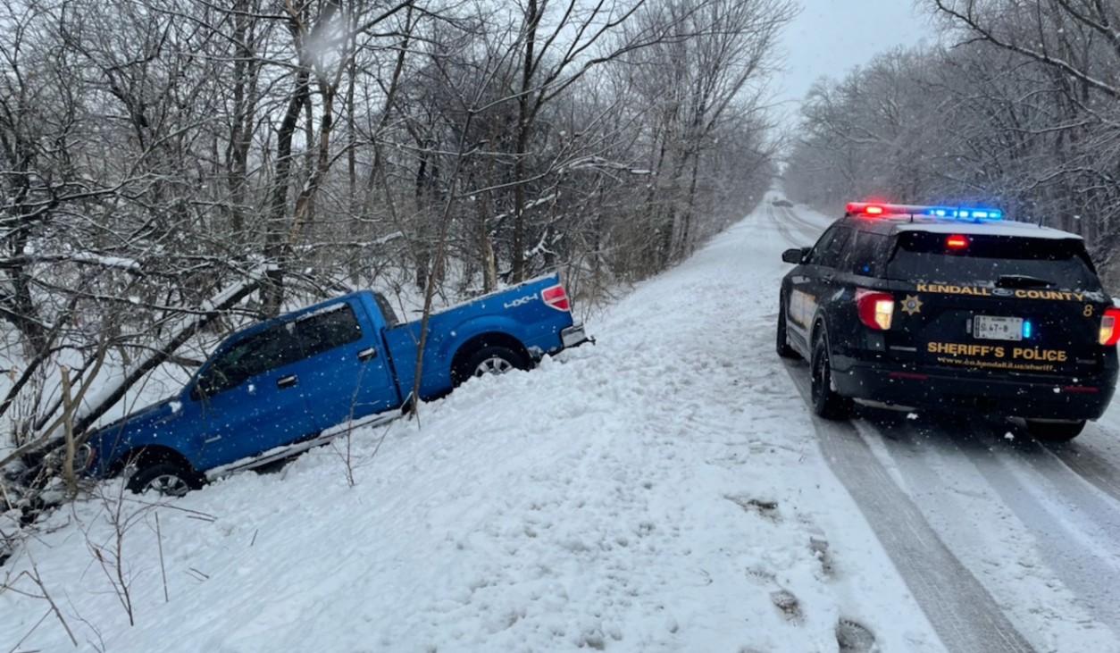 A blue truck is stuck in the snow next to a police car.