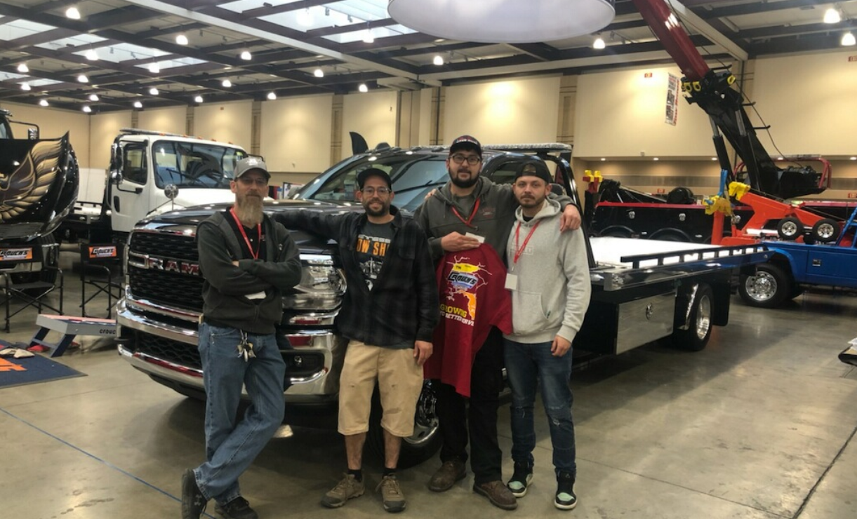 A group of men are posing for a picture in front of a tow truck.