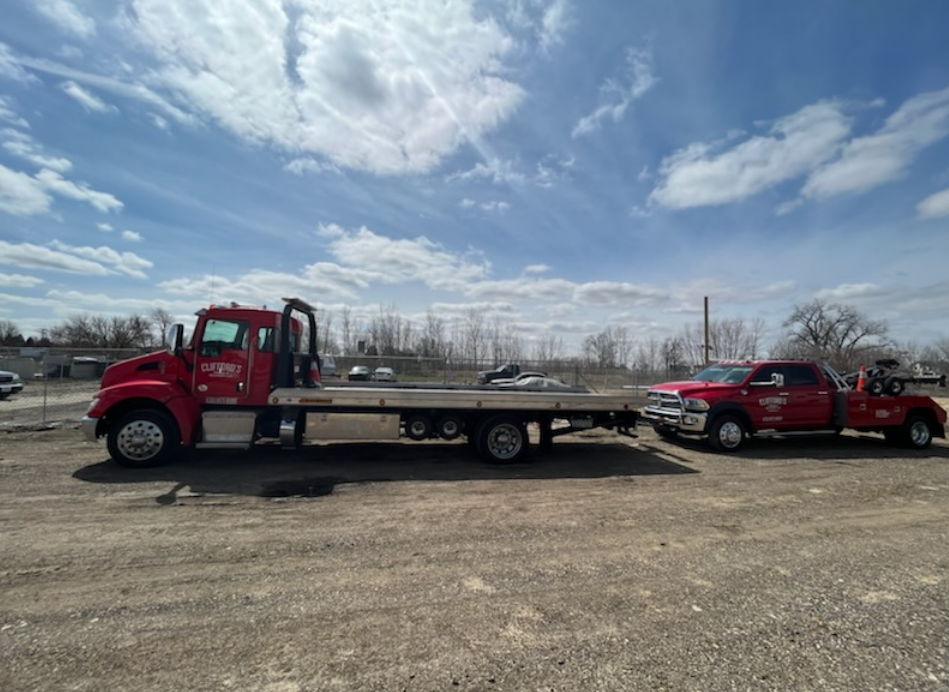 Two red tow trucks are parked next to each other in a gravel lot.
