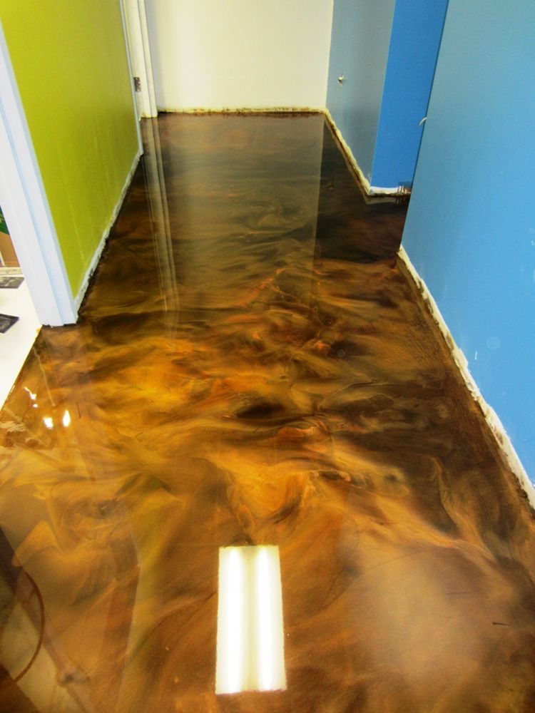 Construction workers in industrial hall applying grey epoxy resin to the floor to create a smooth and durable surface.