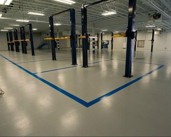 Construction workers in industrial hall applying grey epoxy resin to the floor to create a smooth and durable surface.