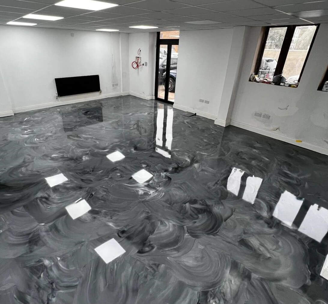 Construction workers in industrial hall applying grey epoxy resin to the floor to create a smooth and durable surface.