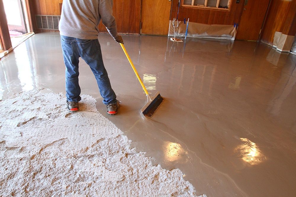 Construction workers in industrial hall applying grey epoxy resin to the floor to create a smooth and durable surface.