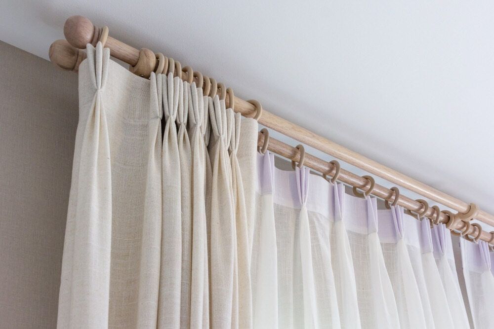 Beige curtains hanging from a wooden rod with gold rings.