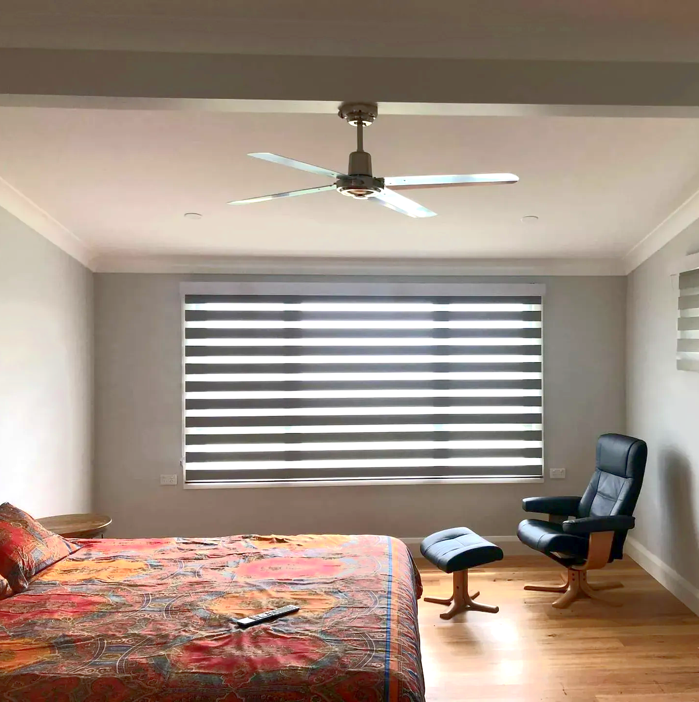 Bedroom with bed, chair, and large window with layered blinds. Ceiling fan present.