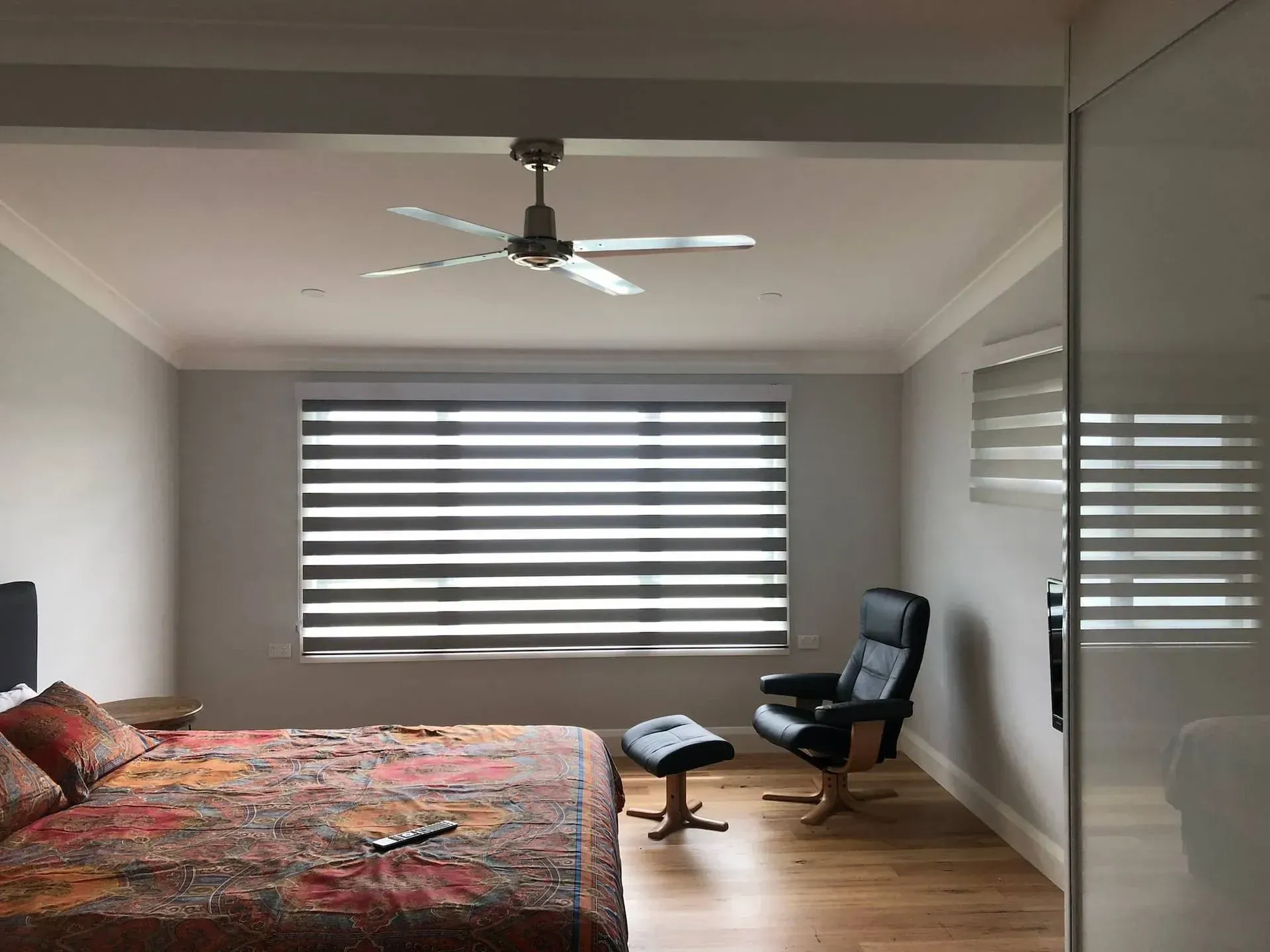 Bedroom with bed, chair, and horizontal striped blinds on the window. A ceiling fan is visible.
