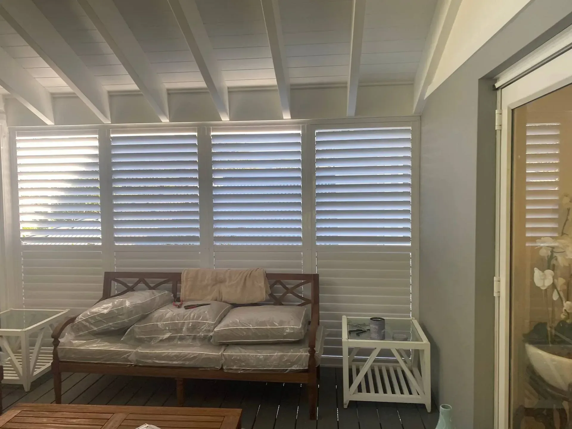 White shuttered patio with sofa, side table, and ceiling beams.