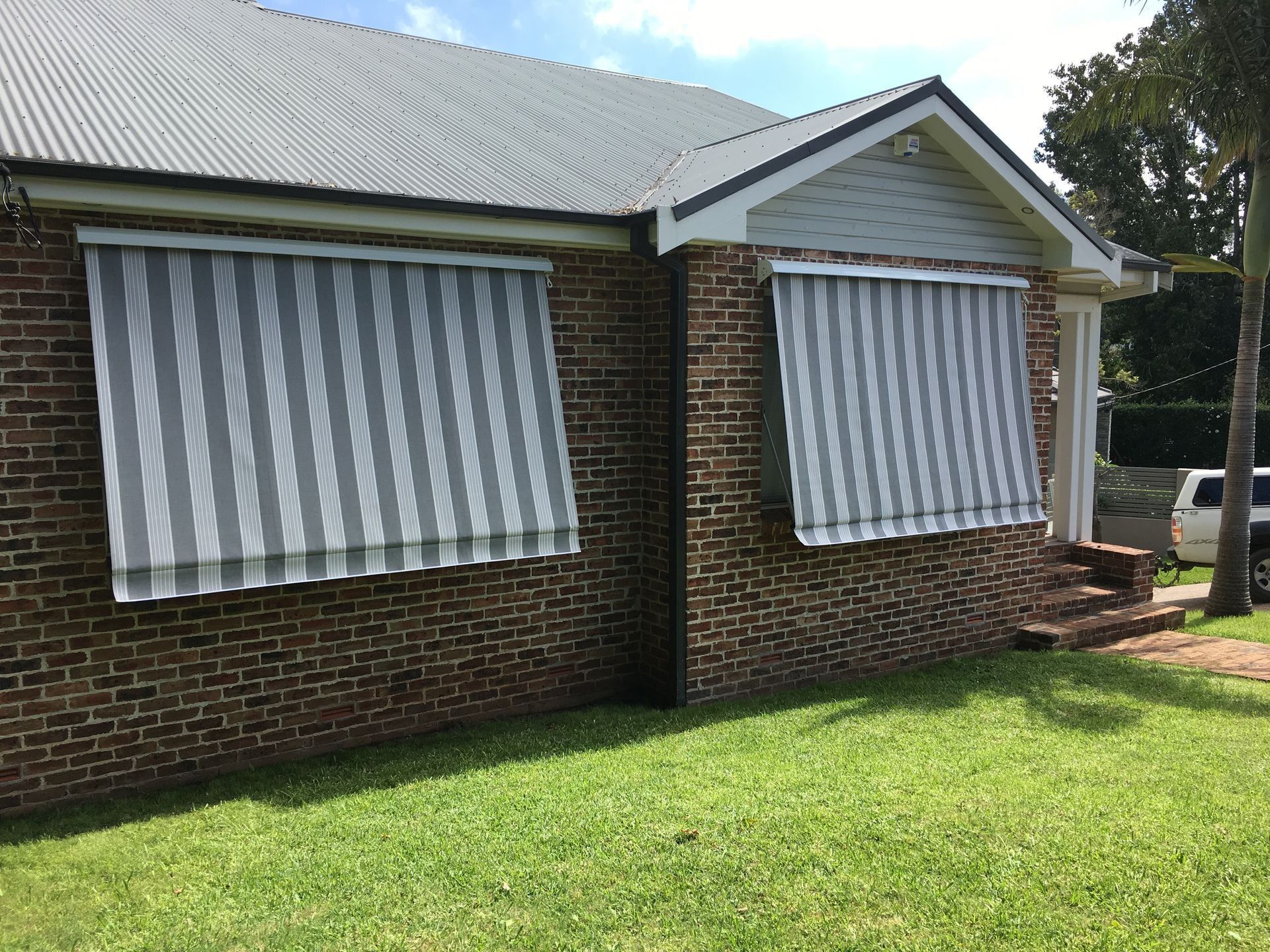 Brick house with two windows covered by striped gray and white awnings.