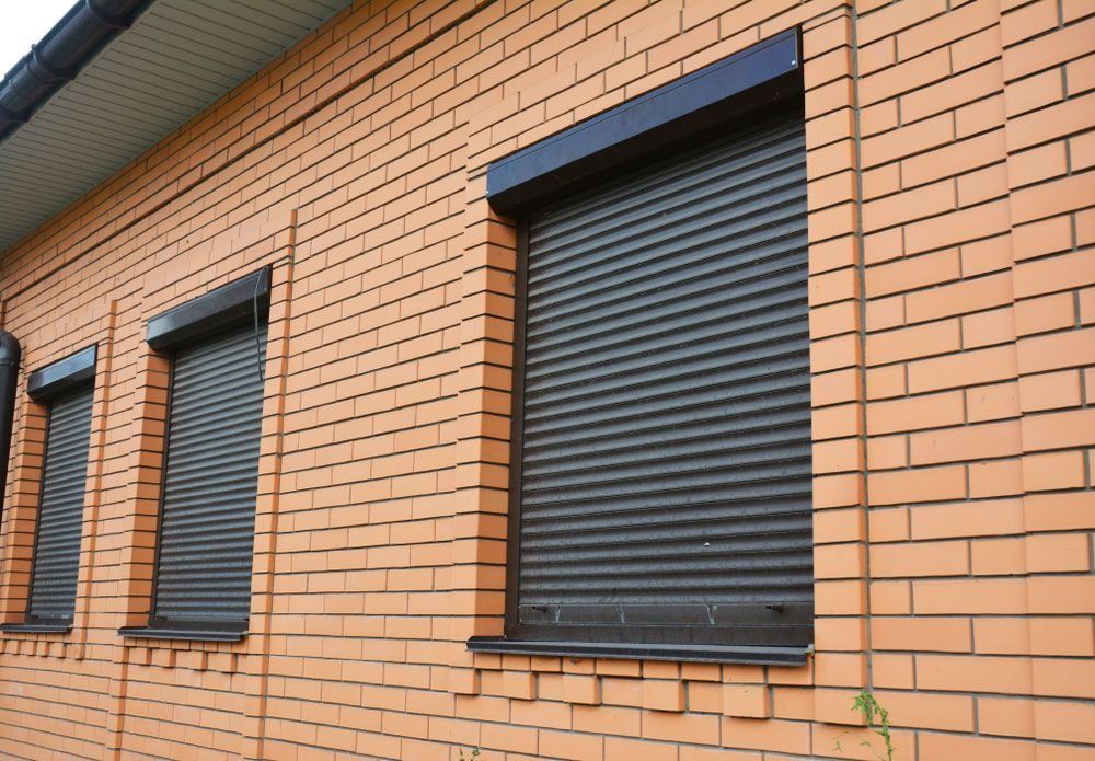 Brick building with three windows, each covered by a closed, dark-colored roller shutter.
