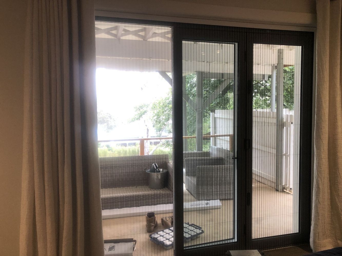 Sliding glass doors with pleated screens, partially open to an outdoor patio with wicker furniture.