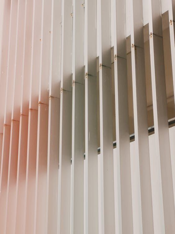 White vertical slats, angled, cast a gradient of shadows with pink and green hues.