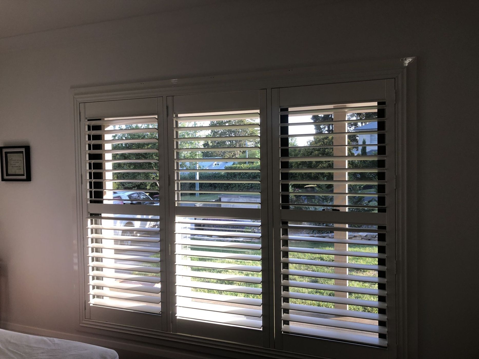 White interior window shutters with open slats, letting in sunlight.