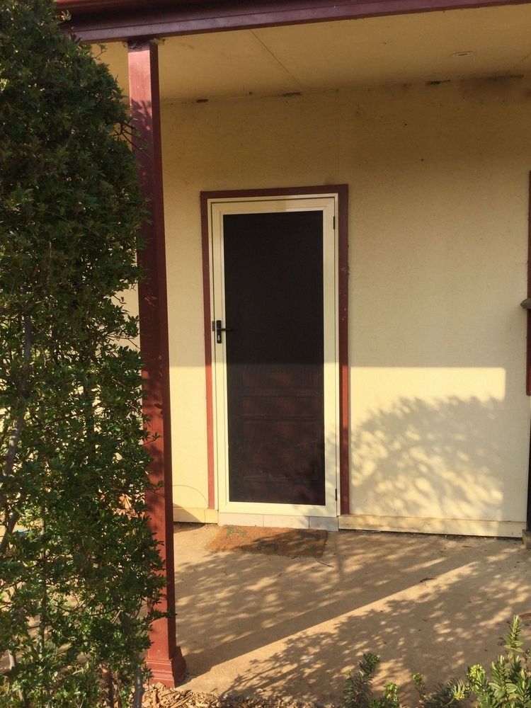 Screen door, cream-colored house exterior, under porch. Dark door with black screen, maroon support column and trim.