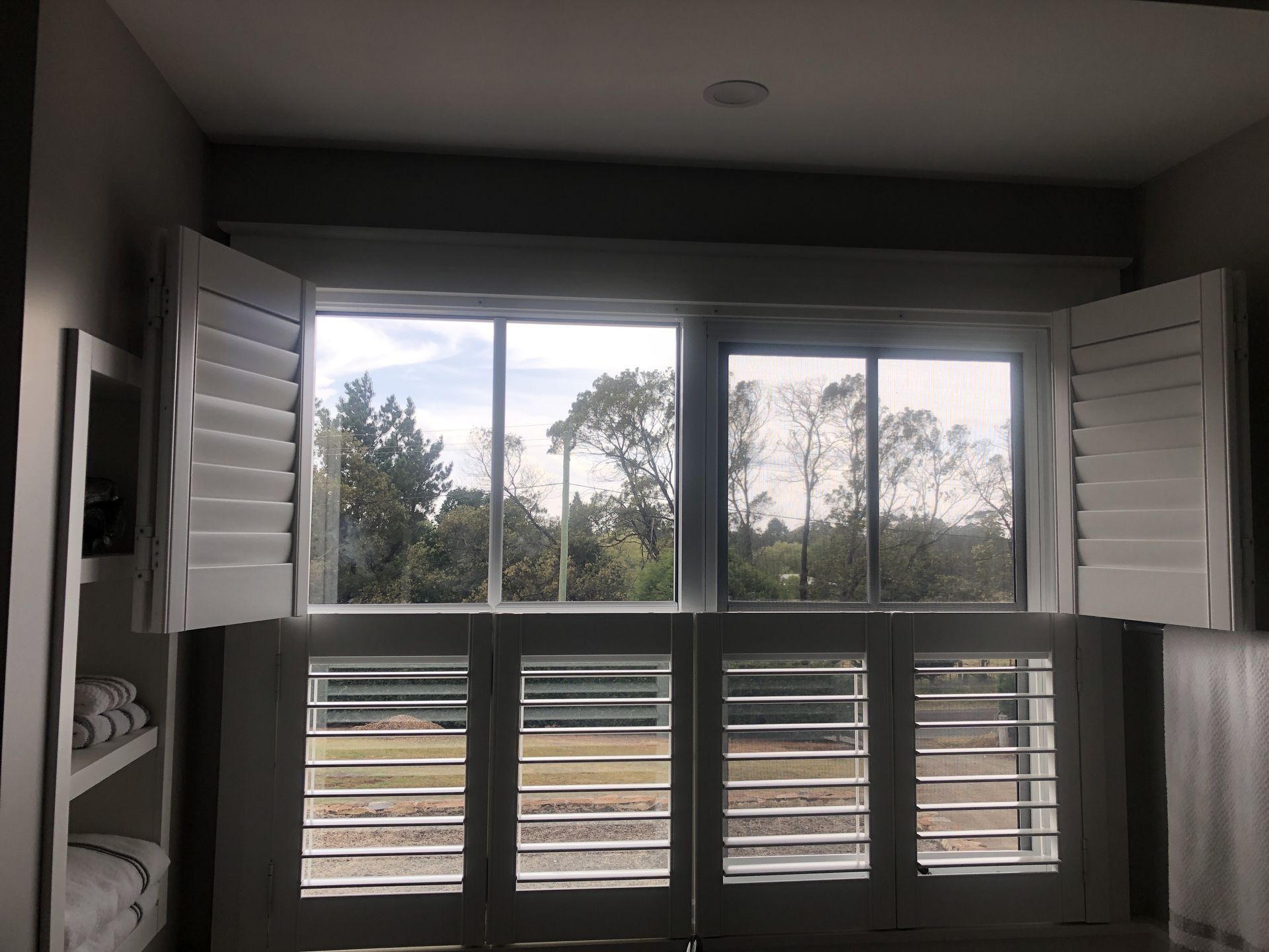 White shutters on a window overlooking a green landscape and trees.