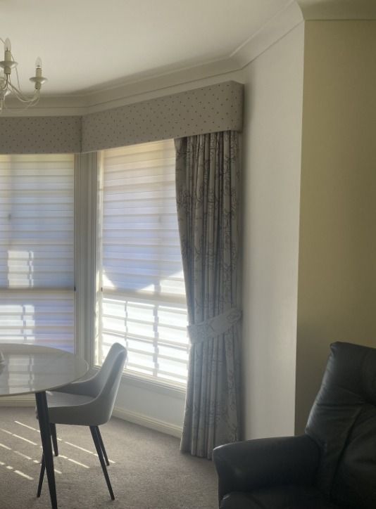 Interior with window, blinds, curtains, and a table and chair. Sunlight streams in.