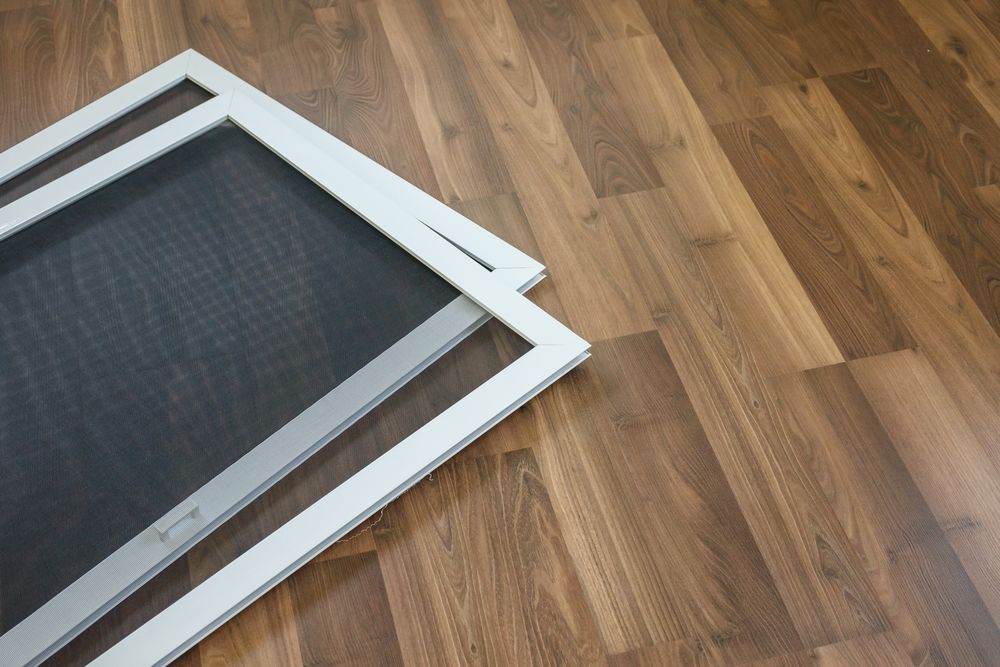 Window with dirty screen and white frame on gray wall.